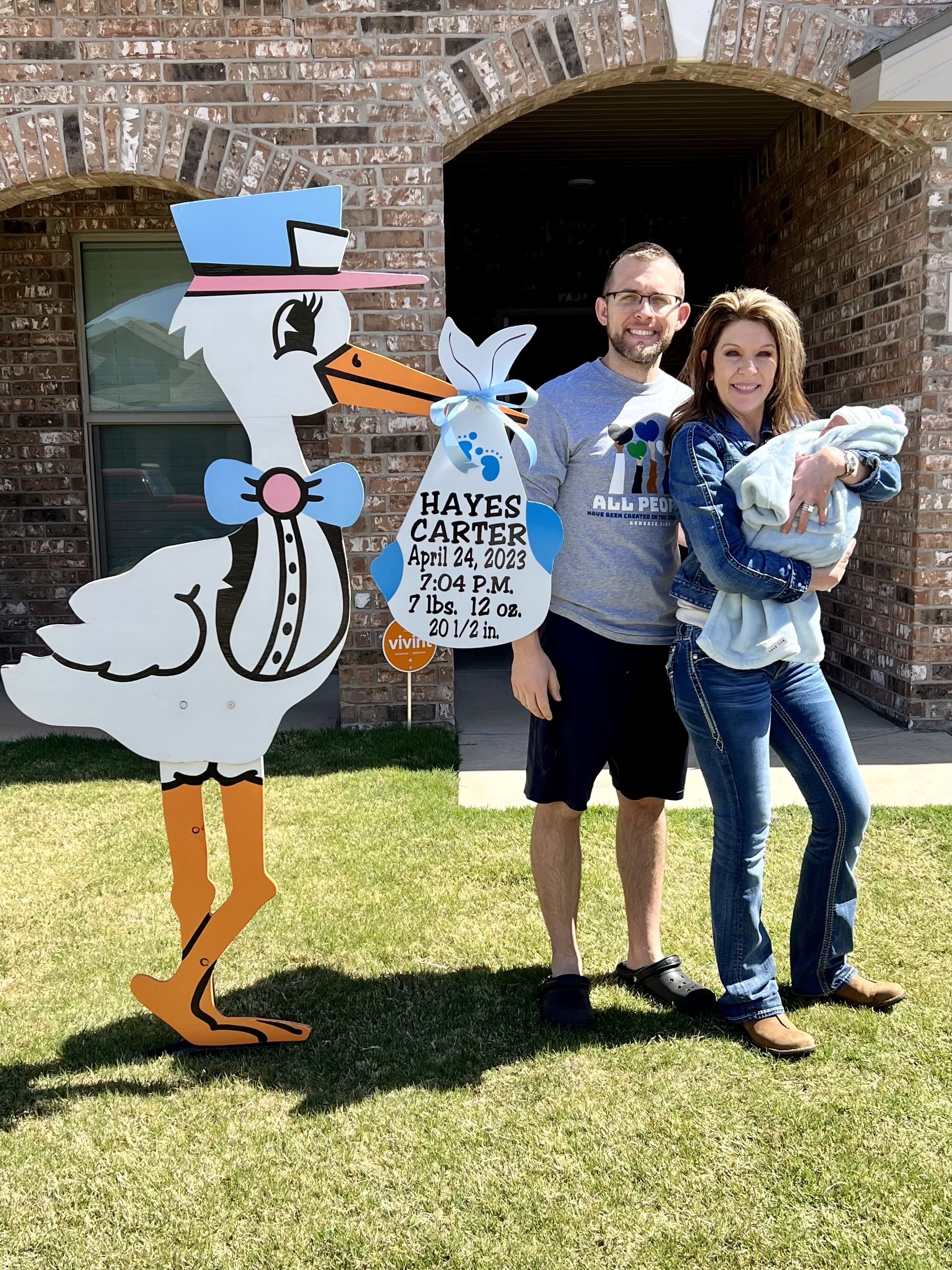 Family with newborn standing beside a personalized stork yard birth announcement sign
